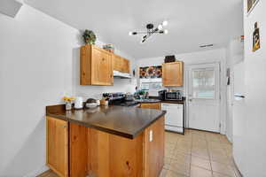 Kitchen with a peninsula, stainless steel appliances, dark countertops, light tile patterned floors, and light wood finish cabinets