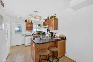 Kitchen featuring wood finish cabinets, a peninsula, white appliances, dark countertops, and a kitchen bar