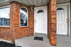 View of exterior entry featuring brick siding and covered porch