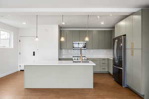 Kitchen with decorative light fixtures, stainless steel appliances, an island with sink, and modern cabinets