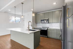 Kitchen featuring stainless steel appliances, a center island with sink, dark wood finished floors, and pendant lighting