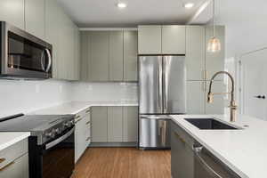 Kitchen featuring stainless steel appliances, light wood finished floors, light stone counters, pendant lighting, and modern cabinets