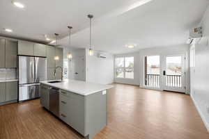 Kitchen with stainless steel appliances, a kitchen island with sink, open floor plan, and light wood-type flooring
