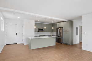 Kitchen with stainless steel appliances, pendant lighting, an island with sink, and light wood-style flooring