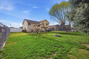 Rear view of house featuring a fire pit, a trampoline, a playground, and a fenced backyard