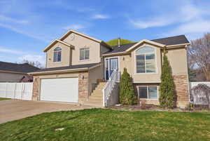Tri-level home featuring stone siding, a garage, stucco siding, and concrete driveway