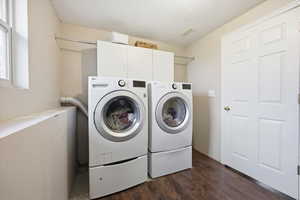 Laundry area with cabinet space, separate washer and dryer, dark wood finished floors, and a textured ceiling