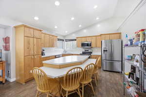 Kitchen with light countertops, stainless steel appliances, a center island, lofted ceiling, and dark wood-style floors