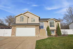 Tri-level home featuring stone siding, an attached garage, concrete driveway, and stucco siding