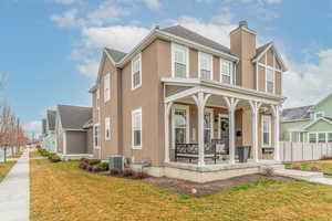 View of front facade with covered porch, stucco siding, a chimney, and roof with shingles