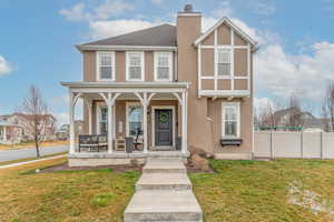 View of front facade featuring stucco siding, covered porch, a chimney, and roof with shingles