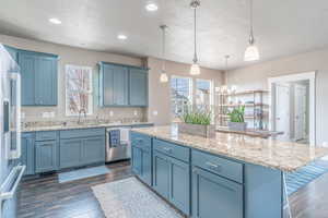 Kitchen with blue cabinets, light stone counters, stainless steel appliances, a center island, and dark wood-style floors