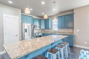Kitchen with blue cabinets, a breakfast bar, stainless steel appliances, and decorative light fixtures