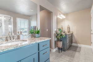 Full bath featuring a textured ceiling, two vanities, light tile patterned flooring, and a stall shower