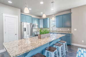 Kitchen featuring blue cabinetry, a breakfast bar area, a kitchen island, stainless steel appliances, and hanging light fixtures