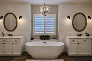 Bathroom featuring two vanities, dark wood finished floors, a soaking tub, and hanging lights