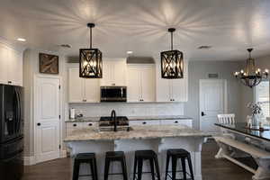 Kitchen featuring hanging lights, black fridge with ice dispenser, white cabinetry, a kitchen bar, and decorative backsplash