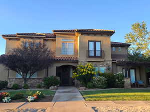 Mediterranean / spanish home featuring a balcony, stucco siding, a tiled roof, stone siding, and a front lawn