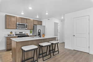 Kitchen with a kitchen breakfast bar, an island with sink, stainless steel appliances, light wood-type flooring, and recessed lighting