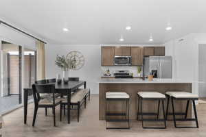 Kitchen with a center island with sink, stainless steel appliances, a kitchen bar, light wood-type flooring, and recessed lighting