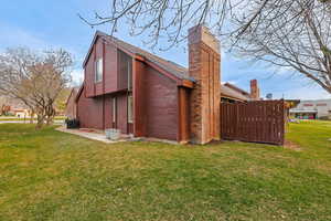 View of side of home featuring a lawn, a chimney, and brick siding