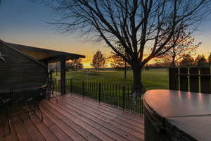 Deck at dusk featuring a hot tub and a yard
