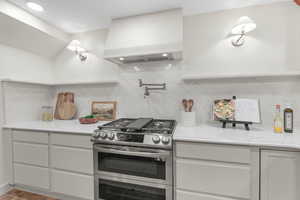 Kitchen with double oven range, white cabinets, light stone counters, and tasteful backsplash