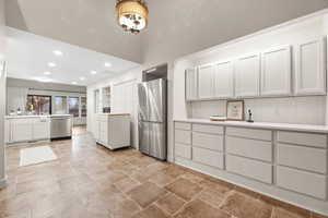 Kitchen with white cabinetry, stainless steel appliances, recessed lighting, light countertops, and light stone finish floors