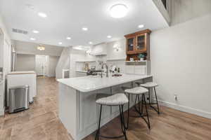Kitchen featuring a breakfast bar area, a peninsula, glass fronted cabinets, recessed lighting, and light stone counters