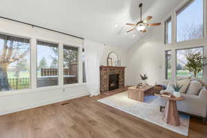 Living area featuring a ceiling fan, light wood-style floors, a fireplace, and vaulted ceiling