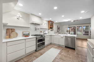 Kitchen featuring a peninsula, stainless steel appliances, a ceiling fan, glass insert cabinets, and recessed lighting