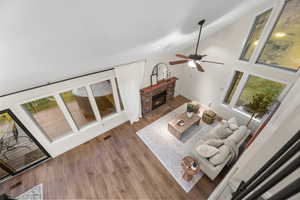 Living room with a glass covered fireplace, wood finished floors, a ceiling fan, and lofted ceiling