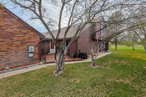 Back of property with a deck, a yard, brick siding, and a shingled roof