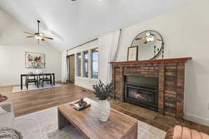 Living area featuring a ceiling fan, wood finished floors, lofted ceiling, and a fireplace