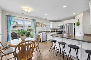 Kitchen with a breakfast bar, dark countertops, white cabinets, stainless steel appliances, and a peninsula