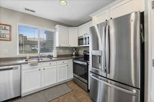 Kitchen with stainless steel appliances, dark countertops, white cabinetry, dark tile patterned flooring, and recessed lighting
