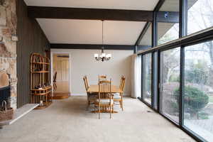 Dining area featuring a fireplace, expansive windows, light carpet, lofted ceiling, and suspended lighting