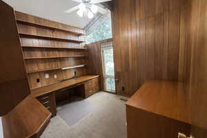 Unfurnished office with built in study area, light colored carpet, a ceiling fan, vaulted ceiling with beams, and wooden walls