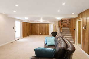 Living area with light colored carpet, wooden walls, and recessed lighting