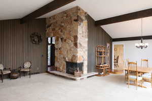 Carpeted living room featuring vaulted ceiling, a fireplace, hanging lights, and wooden walls