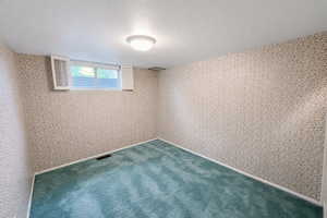 Unfurnished room with a textured ceiling, wallpapered walls, and carpet floors