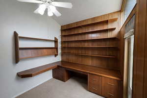 Unfurnished office featuring built in desk, light colored carpet, ceiling fan, and lofted ceiling