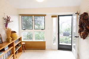 Doorway to outside with brick wall, tile patterned flooring, and healthy amount of natural light
