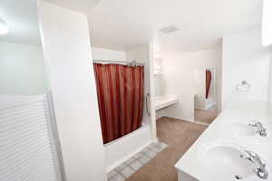 Bathroom featuring double vanity, shower / tub combo with curtain, a textured ceiling, light tile patterned flooring, and light carpet