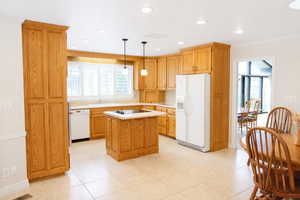 Kitchen with light countertops, white appliances, pendant lighting, a center island, and light tile patterned floors