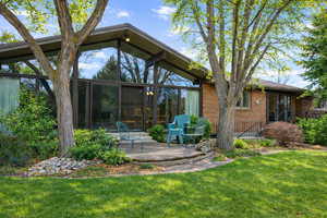 Rear view of property with a lawn, brick siding, a sunroom, and a patio area