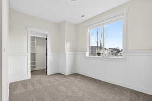 Unfurnished bedroom with a spacious closet, light colored carpet, and wainscoting