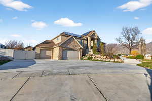Craftsman-style house featuring a gate, stone siding, solar panels, a garage, and concrete driveway