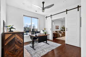 Office area with a barn door, a ceiling fan, dark wood finished floors, and recessed lighting