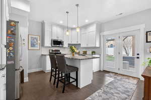 Kitchen with a breakfast bar area, white cabinetry, stainless steel appliances, dark stone countertops, and a kitchen island
